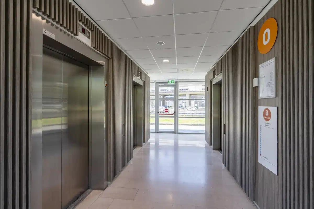 Moderner Aufzugbereich mit drei Fahrstühlen und Holzstruktur im Bright Offices Amsterdam